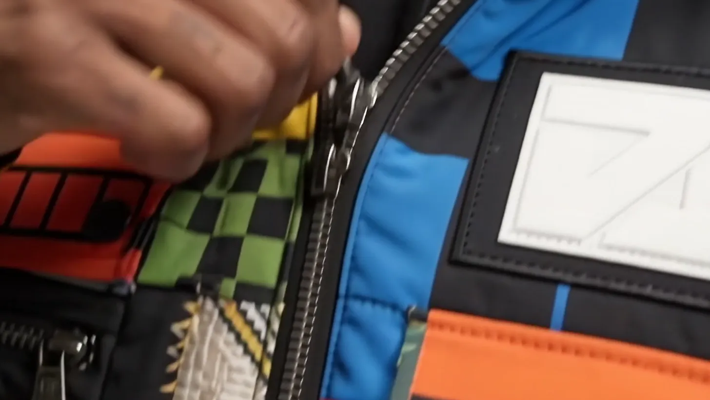 A hand pulling the main zip past a white woven patch